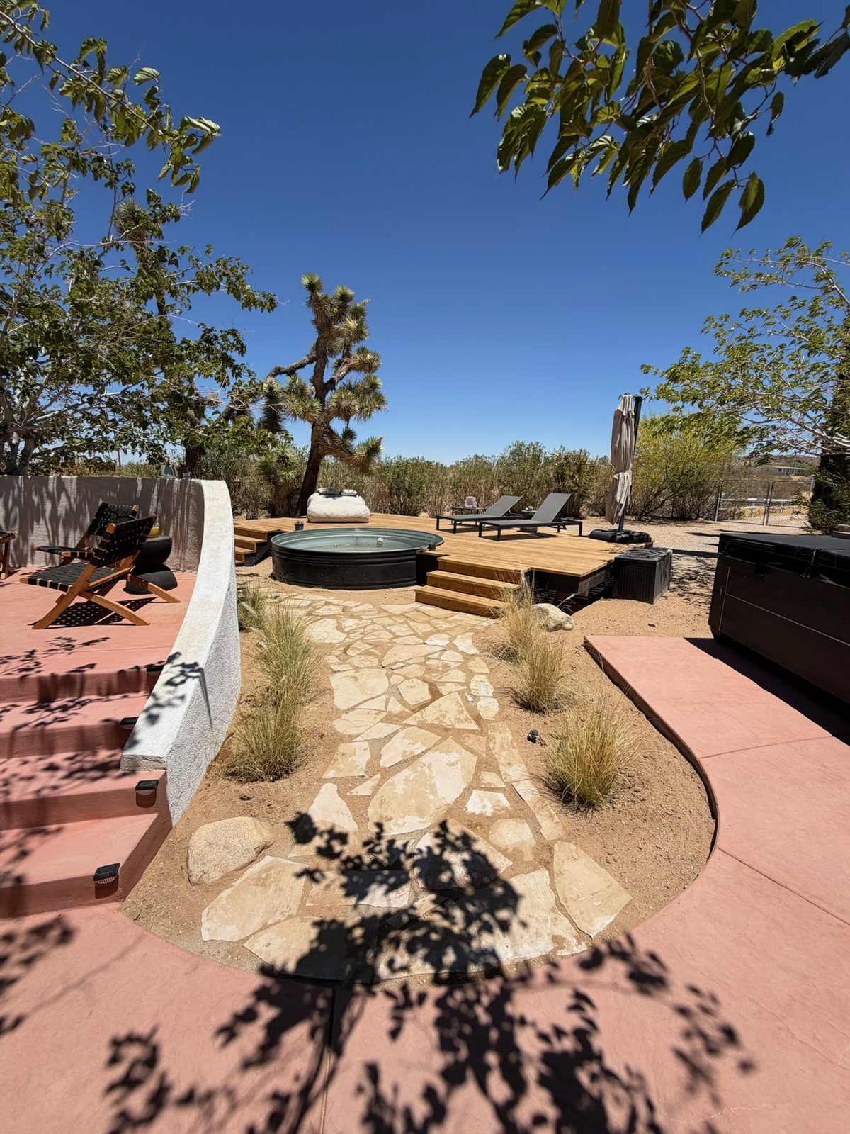 Hot tub area after, a stock tank pool set into a wood deck with a flagstone path and grasses
