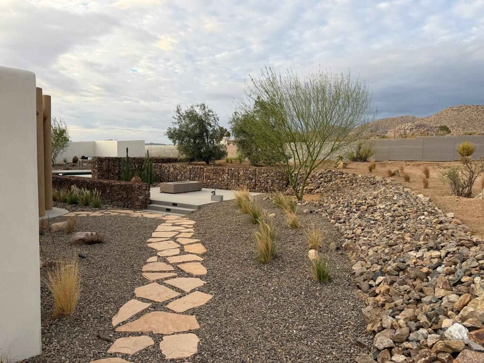 Full desert backyard installation with gabion walls, flagstone path, patio, and native plantings
