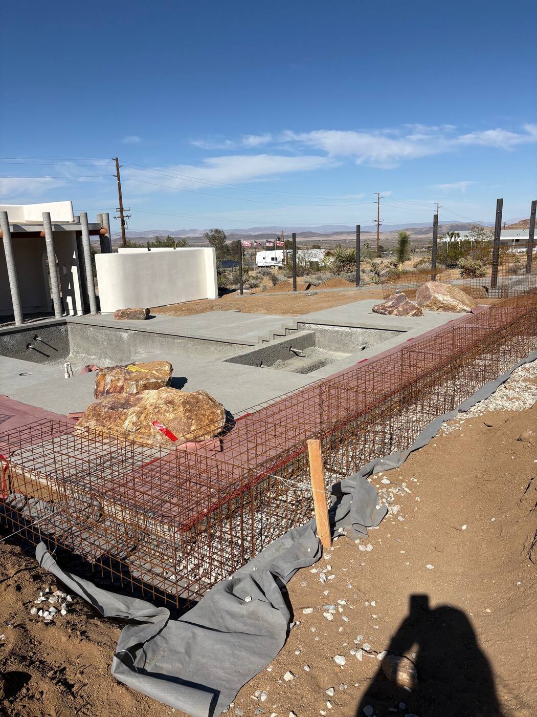 Cage frame running alongside the newly poured pool deck with staged boulders