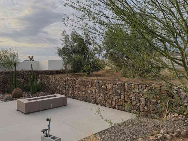 Covered patio and fire pit lounge backed by a gabion retaining wall