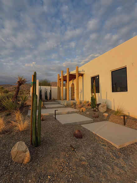 Cactus-lined stone walkway leading to a desert home at sunset